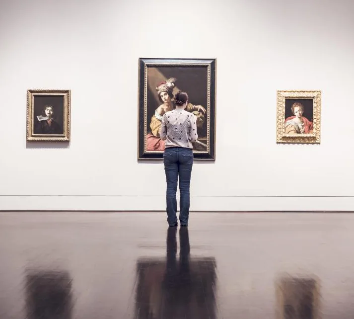 A visitor studying framed paintings on a white gallery wall